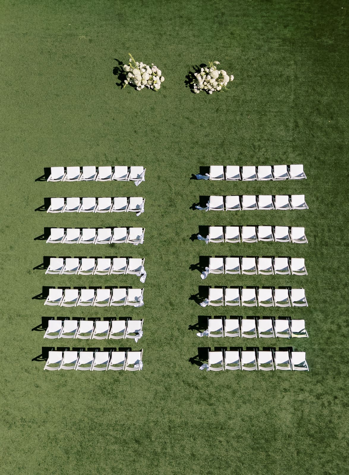 aerial view of wedding ceremony setup with white chairs and a green lawn backdrop with flowers at the center