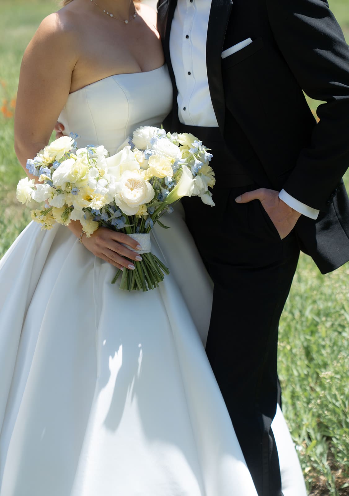 Bride and groom standing together on their wedding day, bride holding a yellow and white bouquet